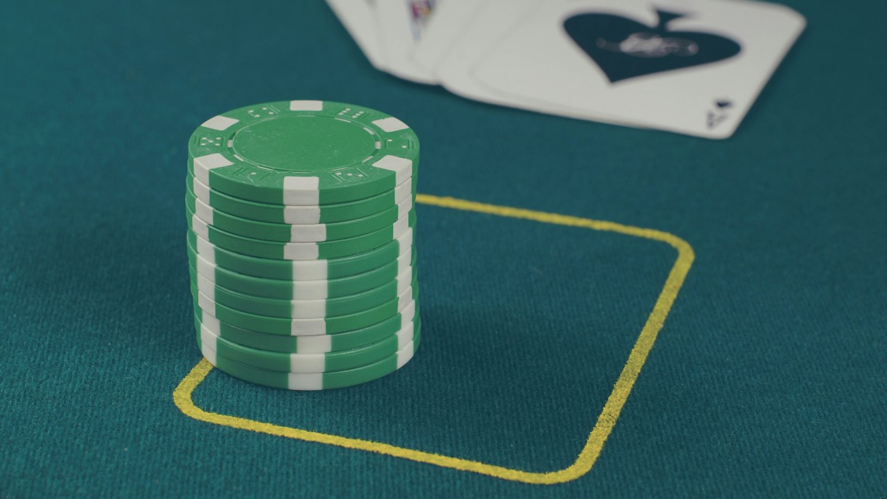 A casino table in close-up: a stack of green chips, the ace of spades and a marked betting box on green felt